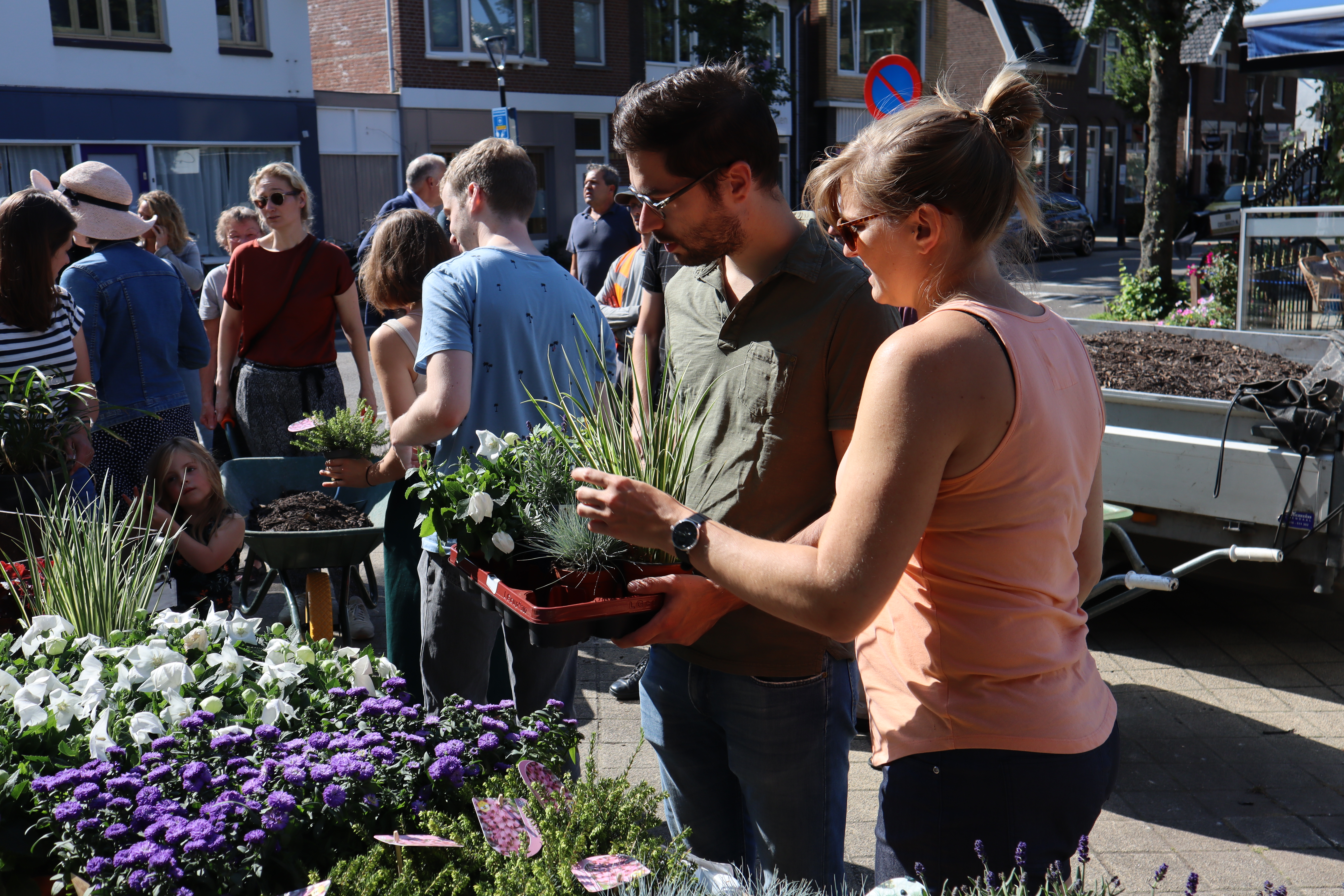 Mensen staan bij een kraampje met allerlei planten. Een meneer heeft een bak met planten in zijn handen