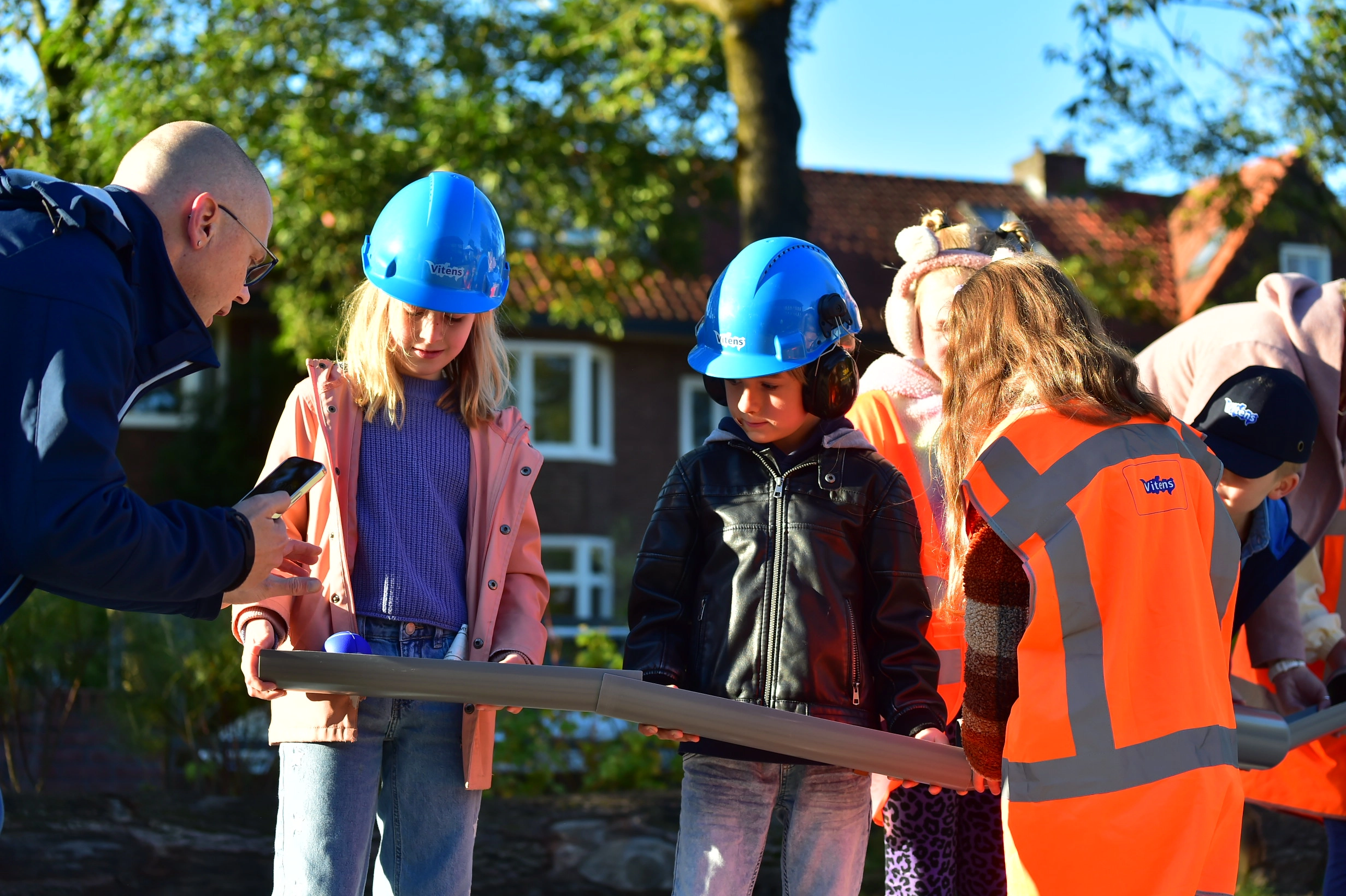 Jonge leerlingen dragen veiligheidshelmen en hesjes tijdens een leeractiviteit over water en techniek.