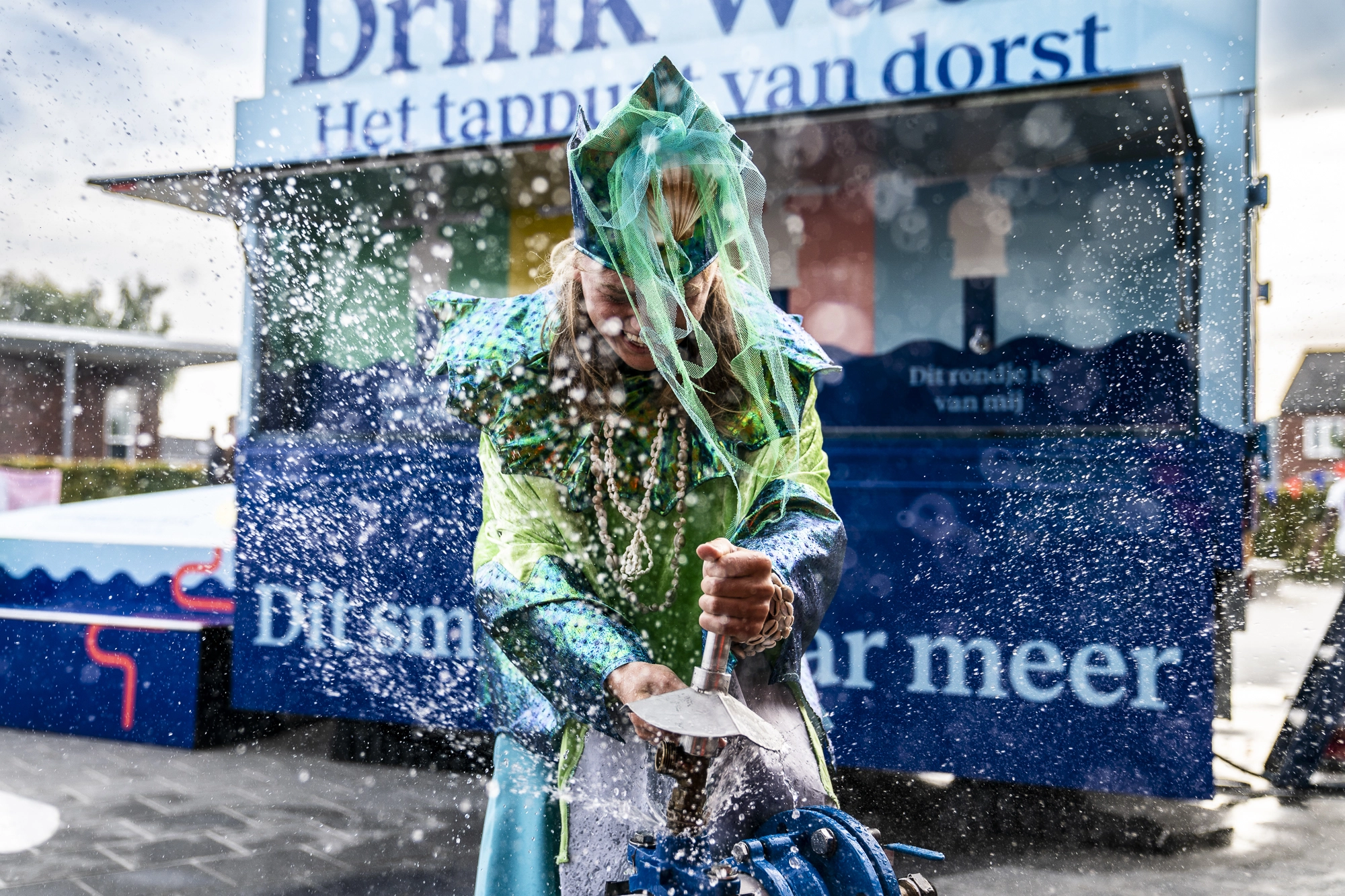 Een persoon in kostuum draait een grote waterkraan open, waarbij water spectaculair opspat tijdens een demonstratie.