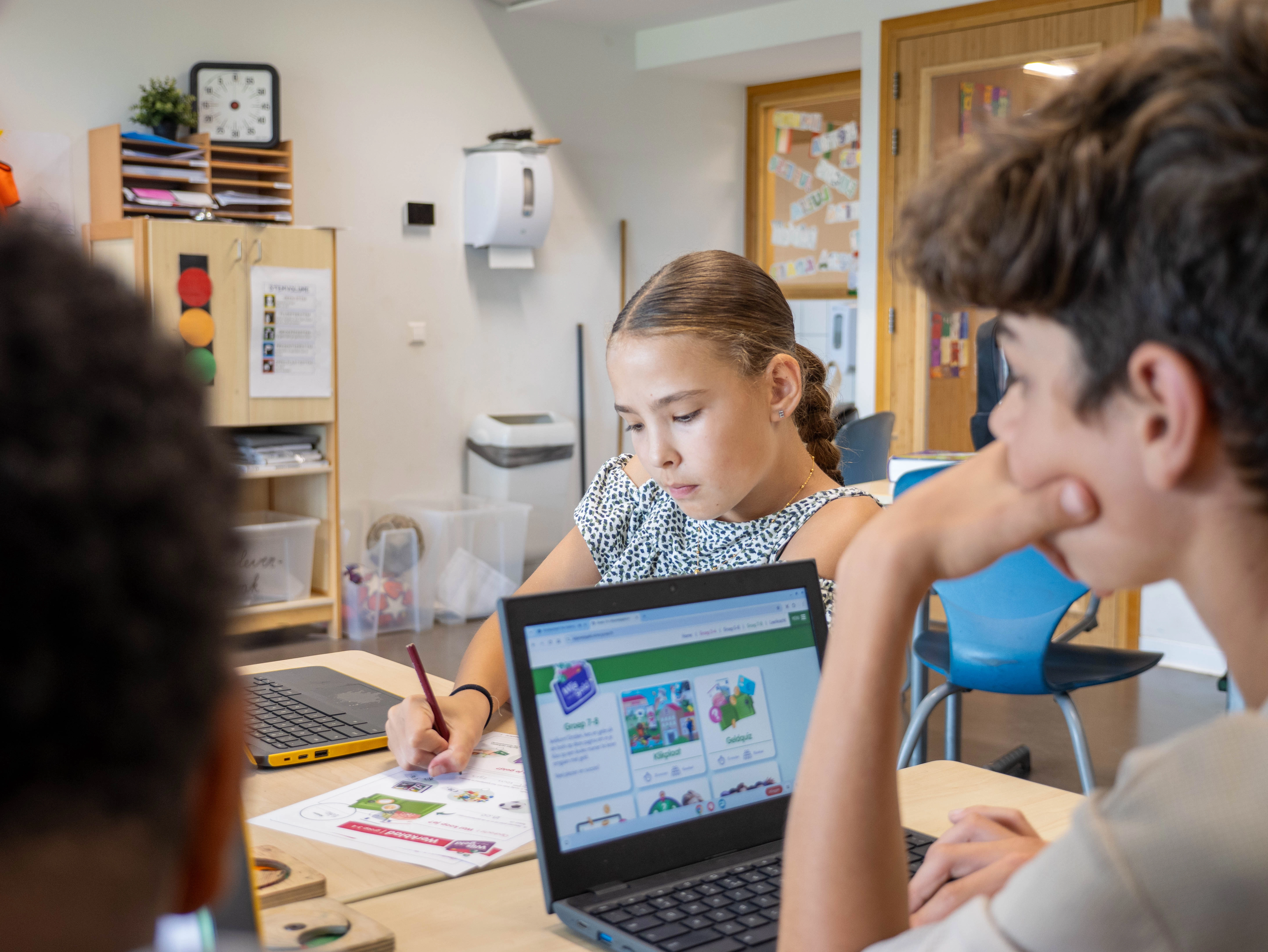 Leerlingen werken individueel op laptops en werkbladen aan opdrachten van Wijzer in Geldzaken in een klaslokaal.