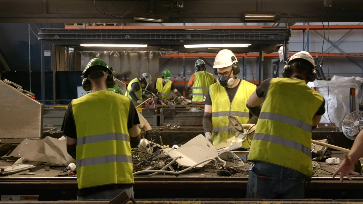 Drie mannen aan het werk in een werkplaats waar elektrische apparaten worden gerecycled. 